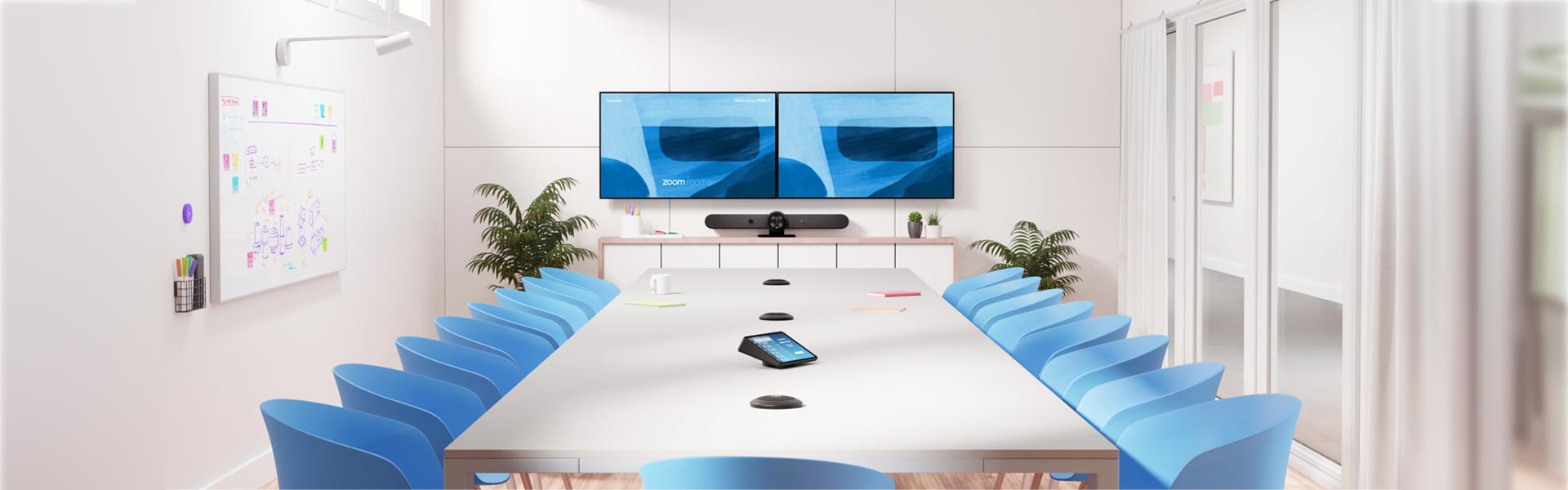 Sala de reunión con dos pantallas, barra de videoconferencia y micrófonos de mesa
